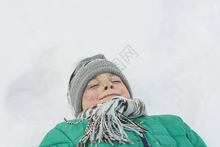 穿着帽子围巾和绿外套的男孩躺在雪地背上图片