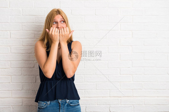 金发女人有点紧张害怕在白砖墙背景上亲手张嘴的图片
