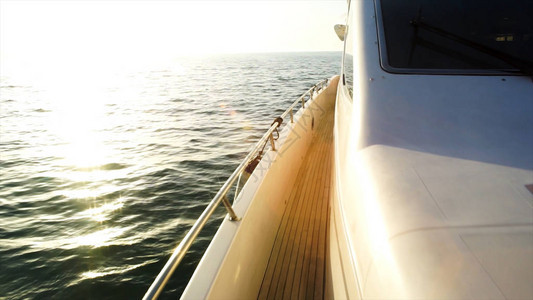 游艇驶向日落带有悬挂帆和柚木甲板的帆船甲板日出时在海水上航行游艇图片