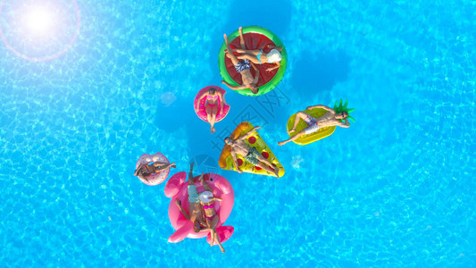 快乐的朋友们享受可充气菠萝披萨法拉明戈西瓜和甜圈漂浮枕头休息室的暑假背景图片