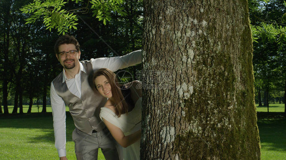 恋爱中的男人和女人在一个令人惊叹的绿色公园中间的树干旁摆姿势新婚夫妇在浪漫婚礼后享受户外照片拍摄年轻夫妇在阳光明媚的花图片