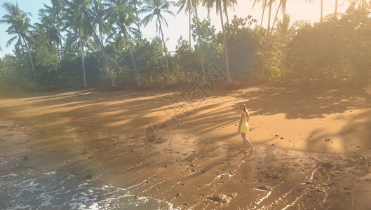 穿着黄色吊带裙的可爱年轻女士正在异国情调的沙滩上愉快地散步图片