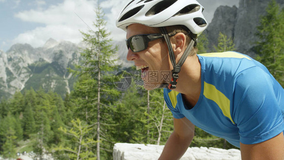 戴着太阳镜的活跃高加索男在阳光明媚的山口上进行激烈的自行车比赛图片