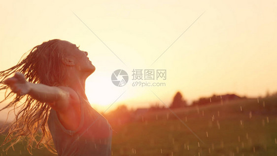 微笑的年轻女子张开双臂在雨中旋转金发白种女孩在令人惊叹的日落时俏皮地跳舞女舞者在图片