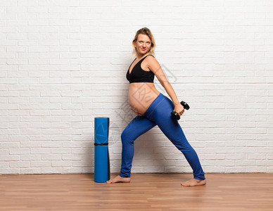 运动金发孕妇在室内锻炼提升体图片
