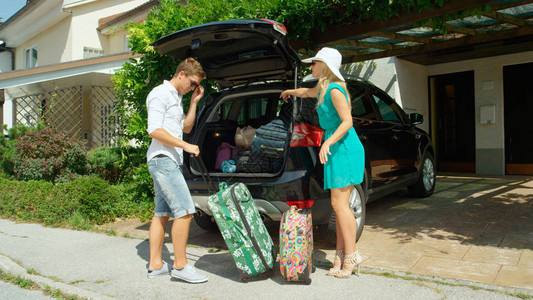 妻子指着她丈夫应该把旅行袋放在靴子里的地方去度假男朋友帮助他的女朋友在一辆黑色SUV的后备箱里收拾太多行李背景图片