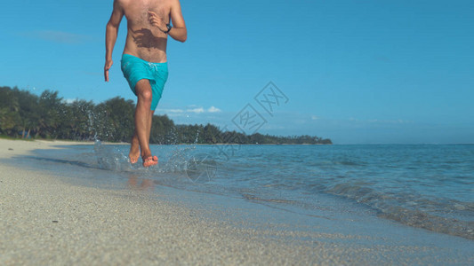 而无法辨认的健美男子沿着壮观的阳光海滩奔跑图片