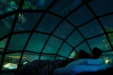 特写年轻的白种人旅游夫妇在斯堪的纳维亚荒野的一座凉爽的玻璃房子里观察夜空女朋友和男朋友在凉爽的玻璃冰屋里享图片