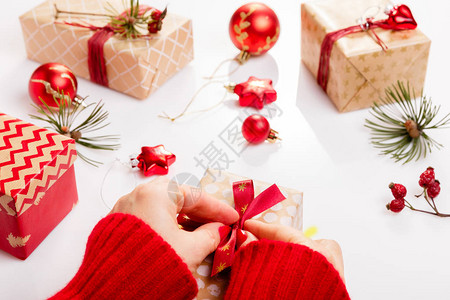 处理包装圣诞礼物白色木桌配红色装饰球蜡烛星女手装饰礼品红丝带新年背景图片