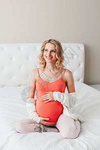 微笑的白色种人白肤金发的孕妇触摸她的腹部的画像期待年轻的中年女士坐在卧室的床上健康快乐的父母图片