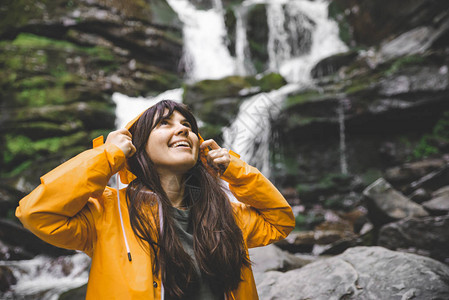背景上有瀑布的黄色雨衣微笑的女人远足概念图片