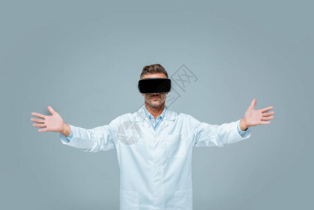 科学家在虚拟现实头盔上握着一些东西在敞开的臂膀中孤立于灰色图片