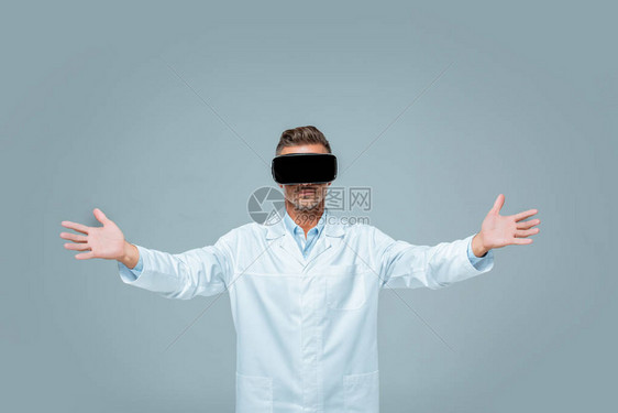 科学家在虚拟现实头盔上握着一些东西在敞开的臂膀中孤立于灰色图片