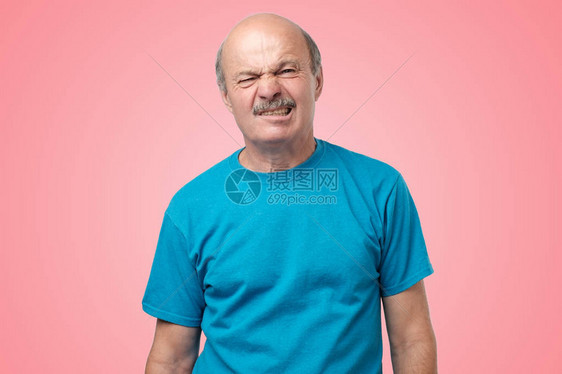穿着蓝色T恤的成熟人对站在粉红背景上的脸部感到厌恶有怀疑图片