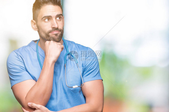 英俊的年轻医生外科医生在孤立的背景下用手托着下巴思考问题图片