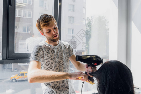 专业微笑的男发型师在沙龙用烘干机图片