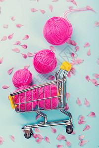 亮粉色羊毛球装满毛线的购物车柔软的棉球和粉红色的花瓣平躺图片