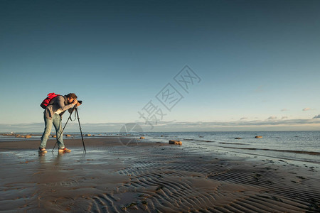 专业旅行摄影师在沙滩上与三脚架站立照片拍图片