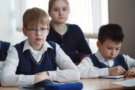 在学校的书桌坐着戴眼镜的年轻小伙将教师的任图片