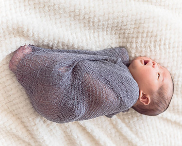 刚出生的亚洲男婴裹着紫色针织马海毛6天大婴儿躺在床上图片