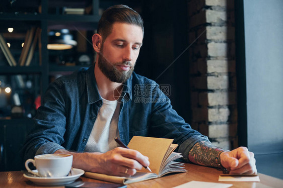 男人手用钢笔写在木桌上的笔记本上在咖啡图片