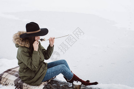 女孩在被雪包围的篝火旁吃油炸棉花糖图片