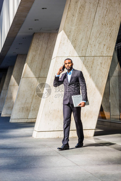 留着胡子的非洲裔美国商人在讲手机旅行在纽约工作穿着黑色西装皮鞋携带笔记本电脑从办图片