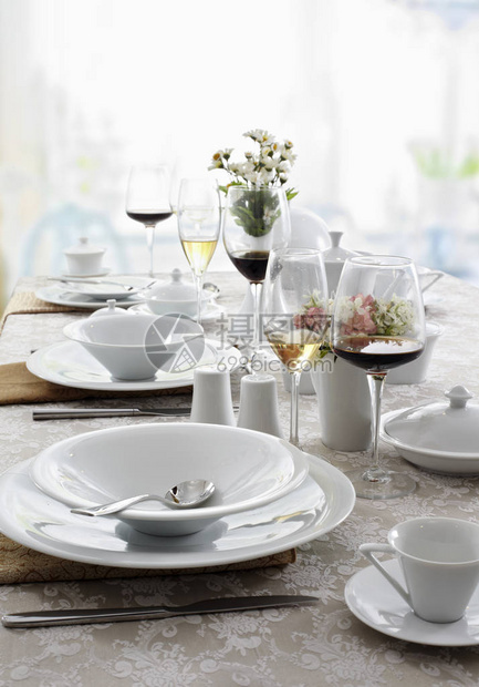 提供白色菜肴餐具和酒杯的餐桌图片