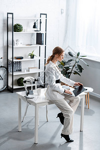 坐在办公桌上和在工作场所使用笔记本电脑的白正式身着白正式服装的图片