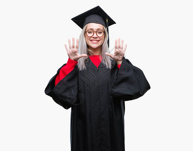 身穿毕业制服的金发年轻女郎在孤立的背景展出和指着十号手指时微笑着自信图片