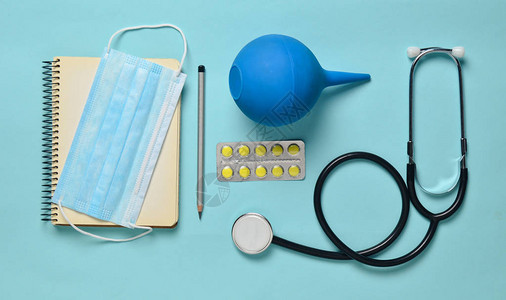 蓝色背景上的医疗设备灌肠剂水泡丸记事本听诊器注射器温度计医学概念图片