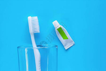 透明玻璃中的白色牙刷与用于清洁蓝色背景牙齿的牙膏图片