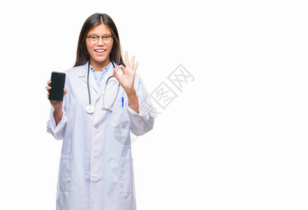 年轻的亚洲女医生拿着智能手机在孤立的背景下用手指做好手势图片