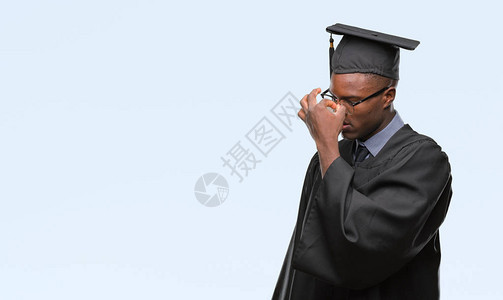 年青的非洲毕业男子在孤立的背景中疲惫地擦鼻子和眼睛图片