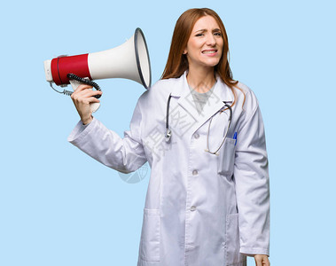 红头女医生用扩音器在孤立的蓝色背景下发出声响背景图片