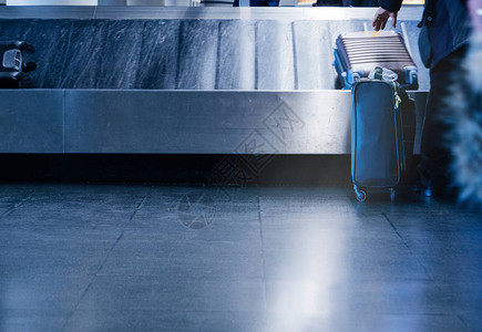 一名男子准备从现代国际机场传送带蓝色拖网图像上取走行李的后图片