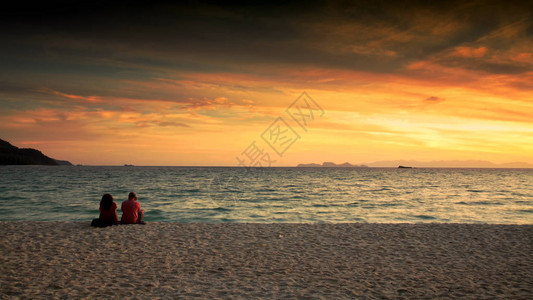 外国夫妇在清晨坐在白沙滩上观看日出时海滨风景图片