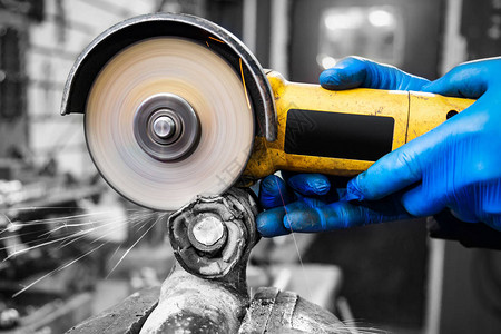 一名年轻的焊工在车间里戴蓝色手套磨床金属角磨机背景图片