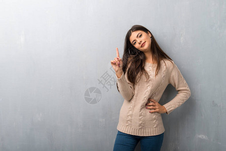 穿着毛衣的少女在古老墙壁上展示并举起一只手指作图片