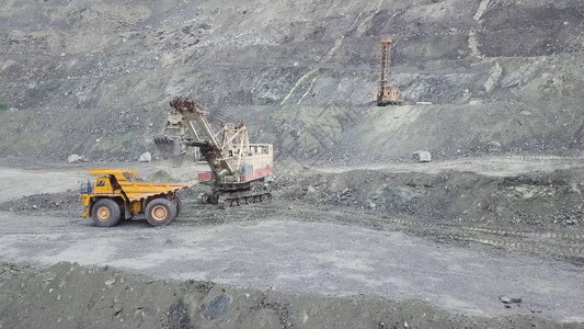 在灰色采石场采矿业装载石矿时的挖掘机和自卸车重型采矿挖掘机将岩石矿装入翻斗式大型采矿卡车图片