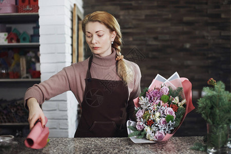 穿着围裙的漂亮中年花女在花廊做花束为了婚礼或周年庆图片