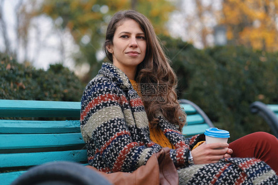 心情不错的年轻美女在秋天喝咖啡的时候坐在长椅上享受好天气图片