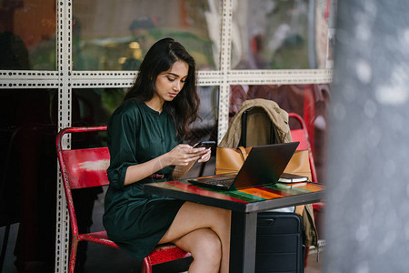 年轻的新加坡印度女在白天在咖啡馆学习或使用笔记本电脑休息时检查图片