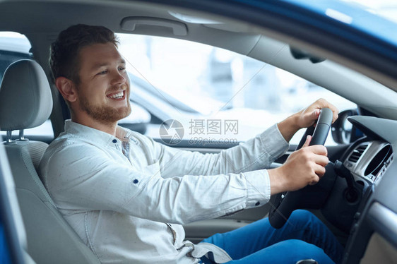 一个快乐的英俊男人在商场尝试一辆新车时愉快地笑着的图片