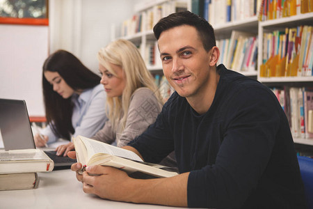 英俊的年轻人在大学图书馆与同学一起学习时对着镜头微笑图片