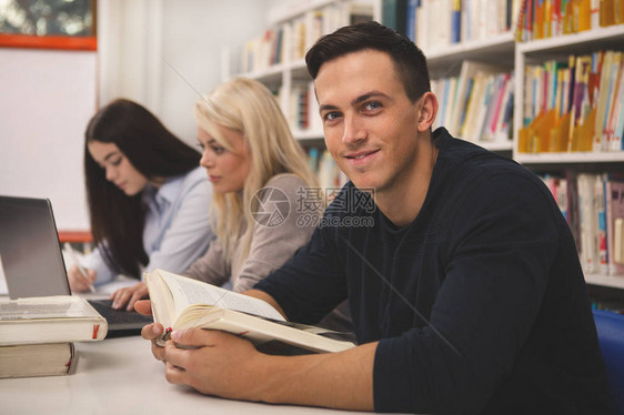 英俊的年轻人在大学图书馆与同学一起学习时对着镜头微笑图片