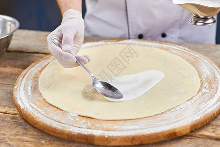 厨师手用勺子在比萨饼的基础上涂抹白酱奶油白酱的特写镜头涂抹图片