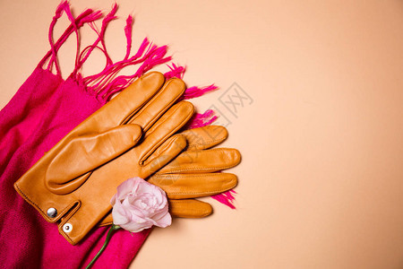 米色背景上粉色围巾上的黄色手套图片