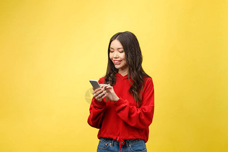 年轻美丽的快乐女人使用智能手机孤立在黄色背景图片
