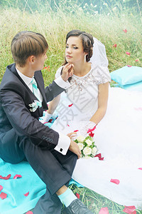 新娘和新郎坐在玫瑰花瓣的绿草地上图片